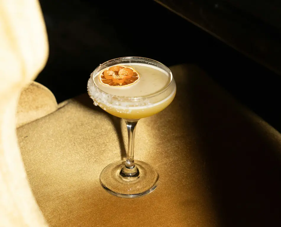 Cocktail in a coupe glass with a salted rim and a dried citrus slice
