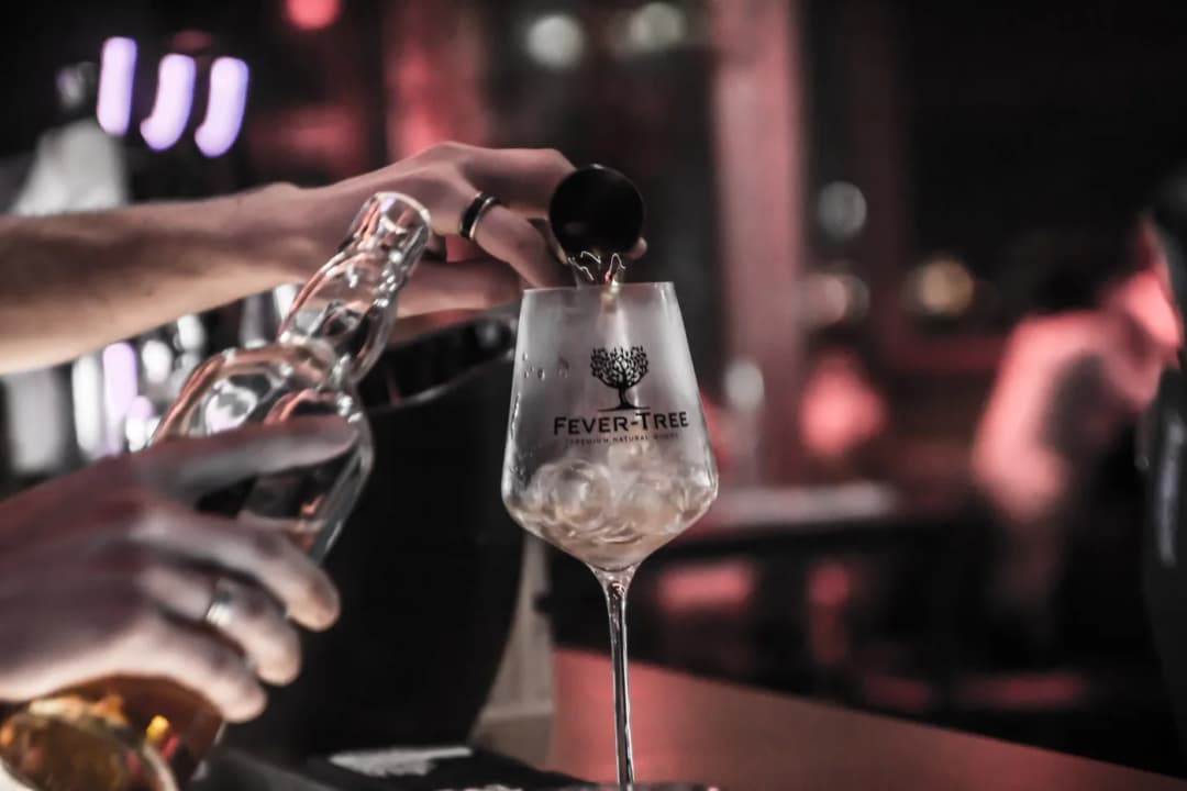 A drink being poured into a glass with ice cubes at the bar